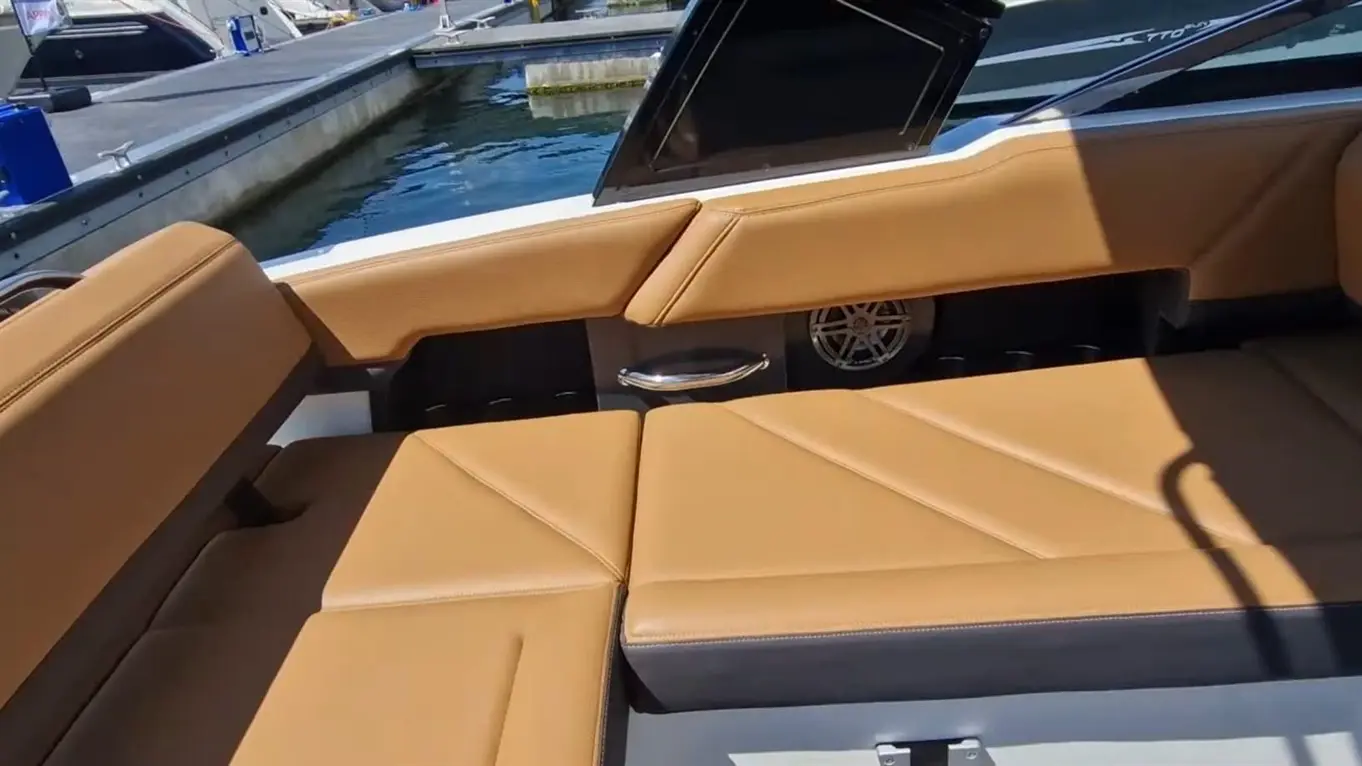 A spacious boat interior features stylish tan cushions and a sleek design, with glimpses of the marina in the background.